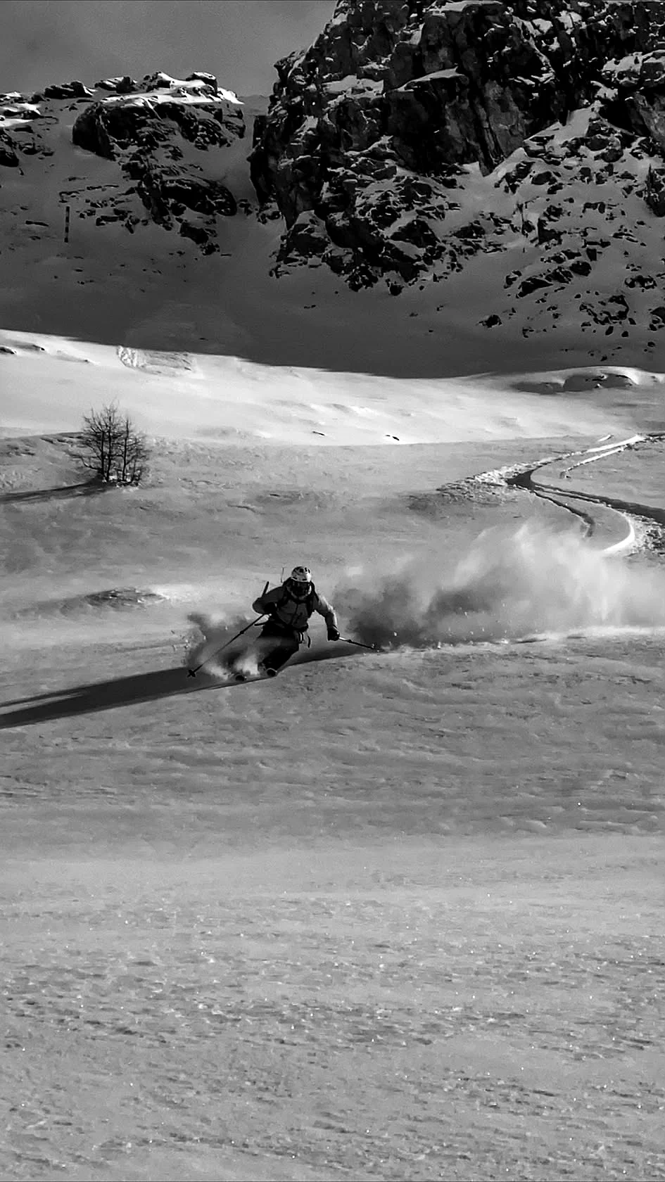 Skieur seul en descente hors-piste sous un rocher, tracé courbe en poudreuse